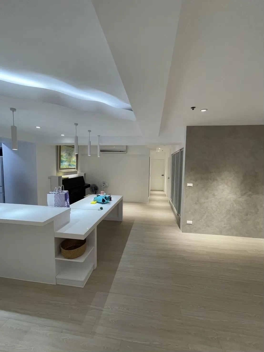 現代住宅開放式公共空間設計，結合白色中島與淺木色地坪，透過流線型天花造型與間接照明營造空間層次，以高 CP 值材質選擇有效控制裝潢預算，兼顧美觀與實用機能。